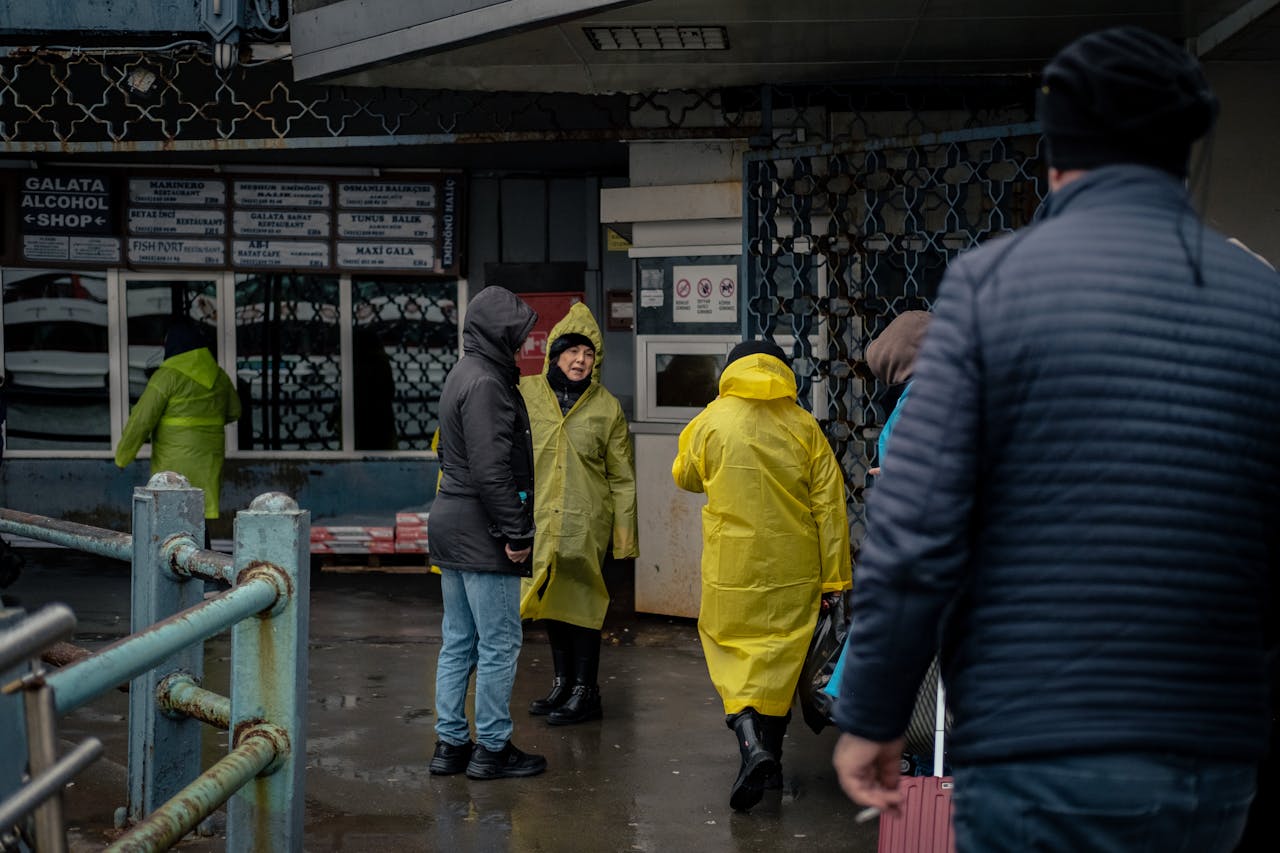 about-img Group of people wearing raincoats walking outside a street market shop on a rainy day.
